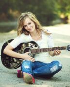 Woman sitting outdoors playing acoustic guitar